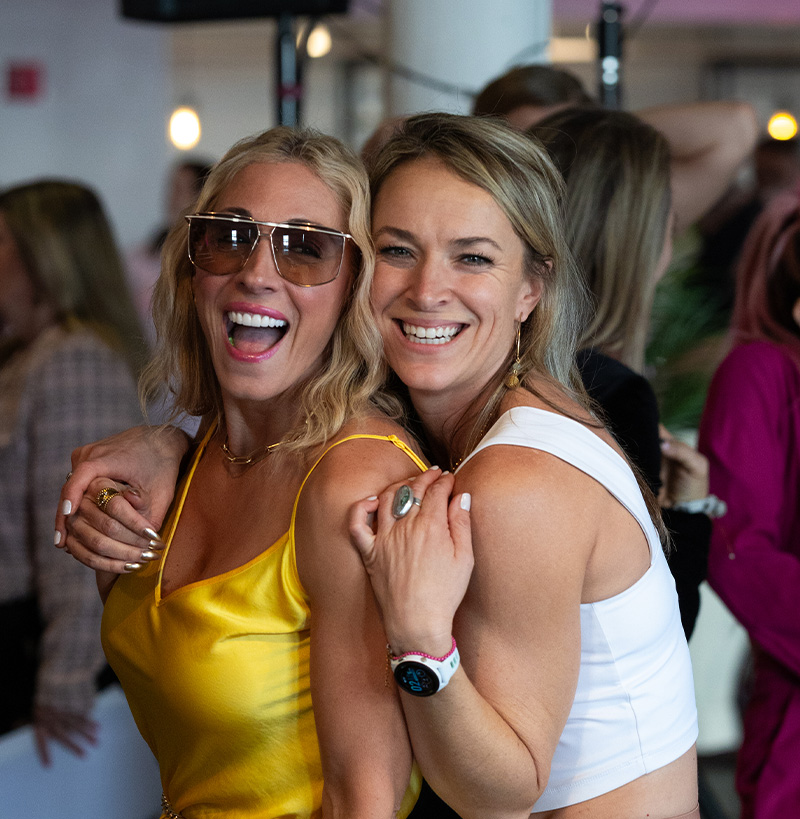 Two women smiling and embracing at a Pause Breathwork Women & Wealth event